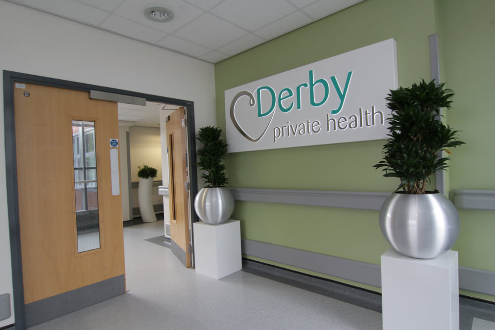 Entrance to Derby private health clinic. Light green wall, sign, and two plants.
