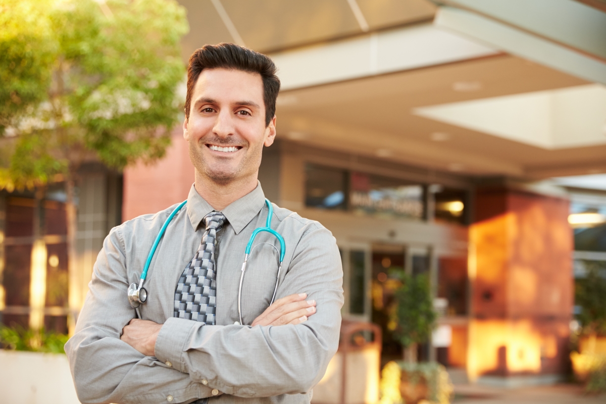 A happy medical professional smiling outside a clinic with his arms crossed